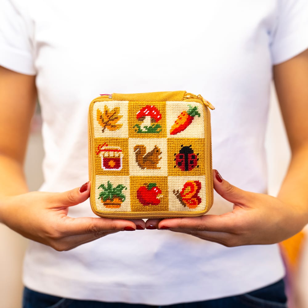 A maker holding the finished FALL HARVEST CHARMS needlepoint pouch