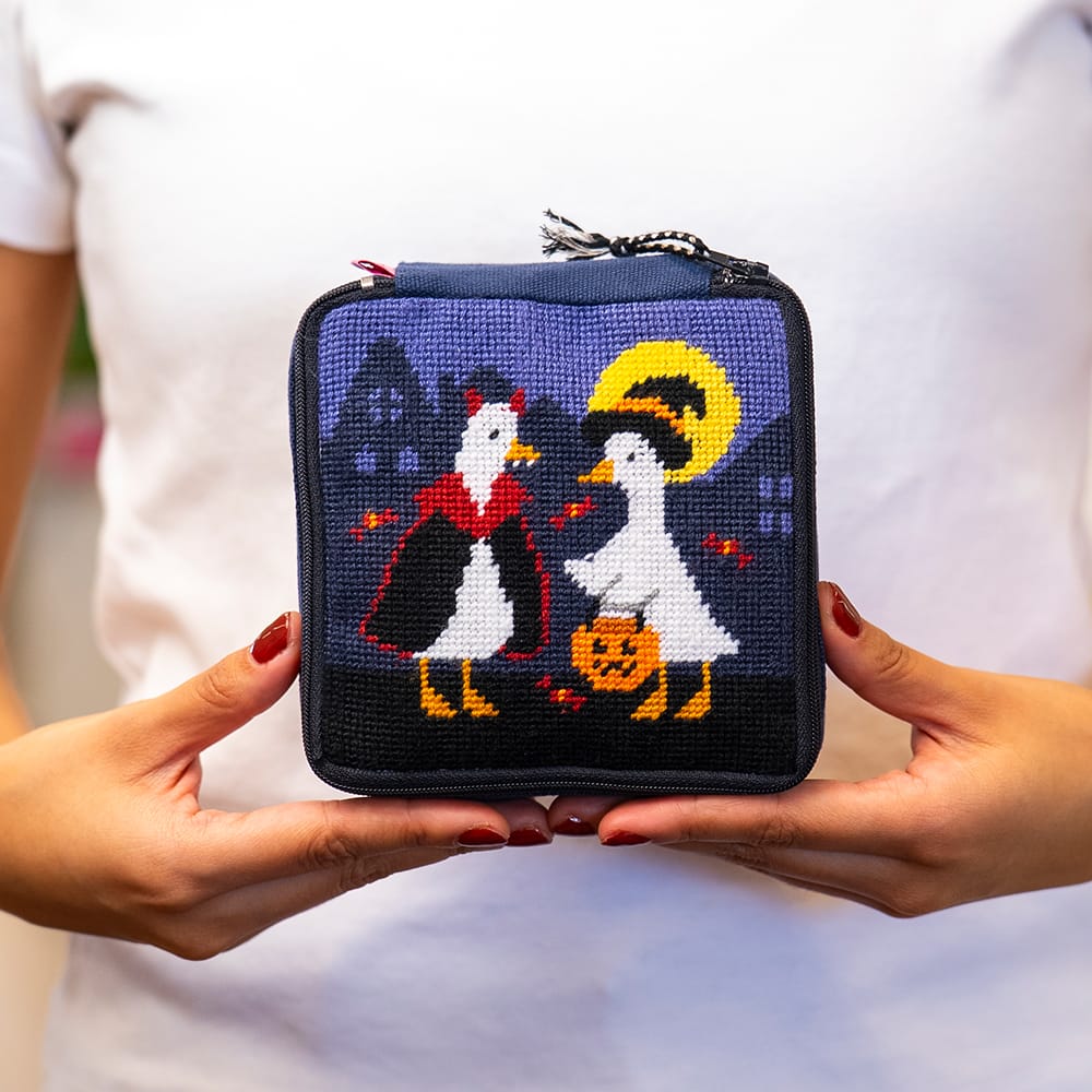 A maker holding the finished TOIL AND TROUBLE needlepoint pouch