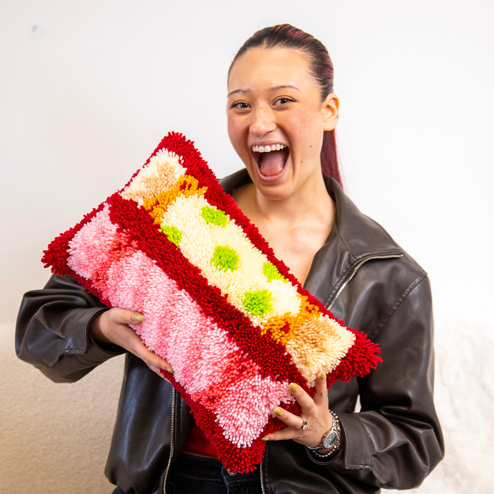 Craft Club CHRISTMAS CRACKERS - Latch Hook Cushion Kit — smiling model holding the finished Christmas cracker cushion