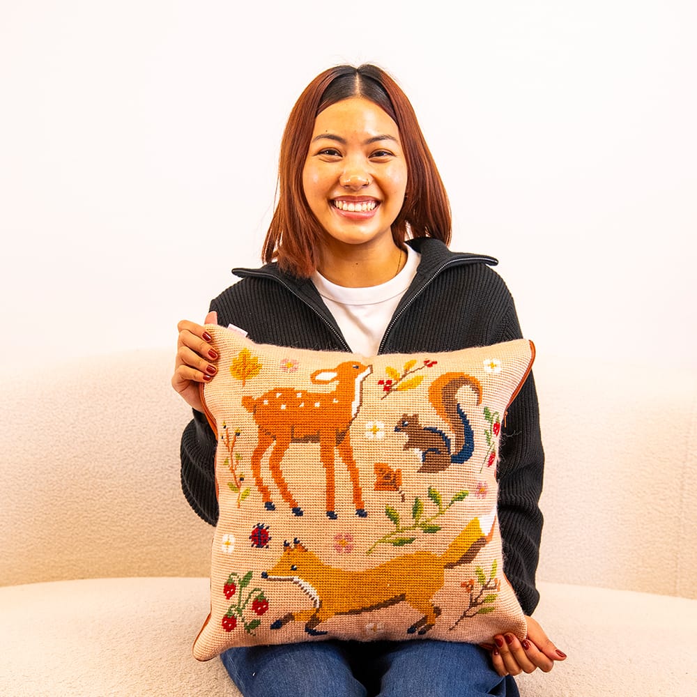 A maker holding the finished FALL FRIENDS woodland needlepoint cushion