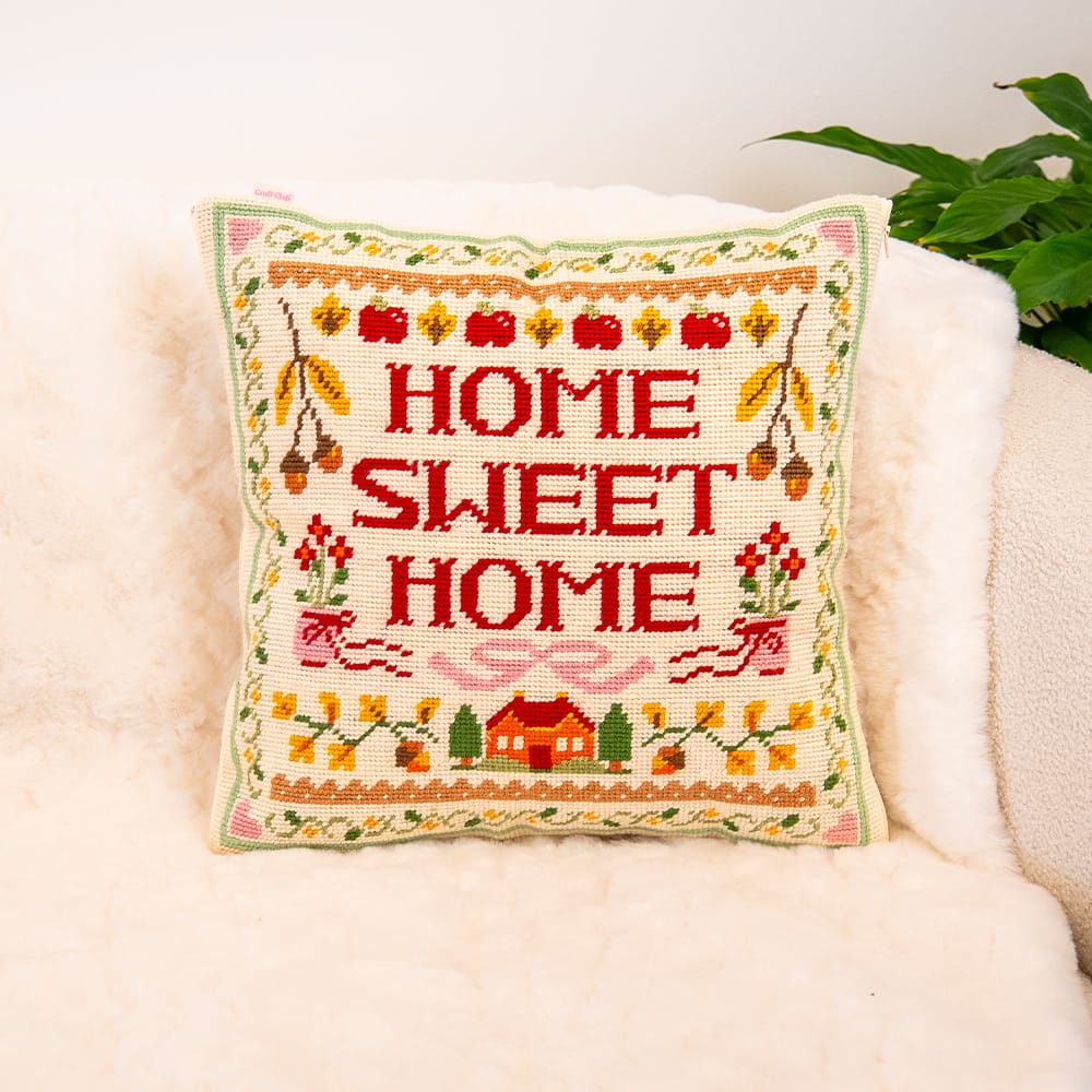 HOME SWEET HOME sampler needlepoint cushion finished and styled on a cream sheepskin armchair