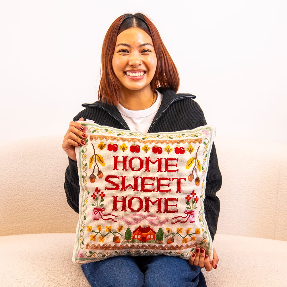 A maker holding the finished HOME SWEET HOME sampler needlepoint cushion