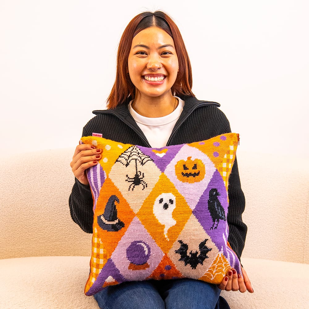 A maker holding the finished SPOOKY TROVES needlepoint cushion