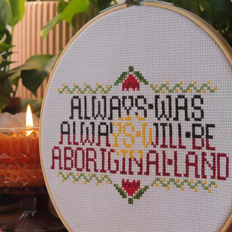 Craft Club Co ALWAYS WAS, ALWAYS WILL BE Cross Stitch Kit. A close up, showing the details of the 'X' stitches and the fabric. There is a candle behind the piece.