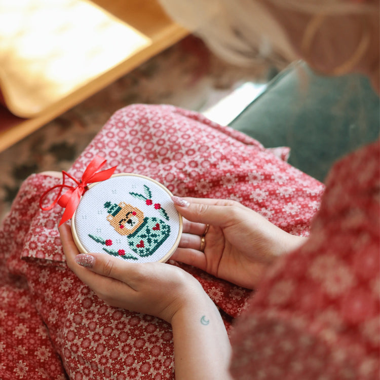 Craft Club Co CHRISTMAS MINI ORNAMENTS Cross Stitch Kit. Looking over a persons shoulder, you can see she is holding the bear cross stitch ornament in her hands.