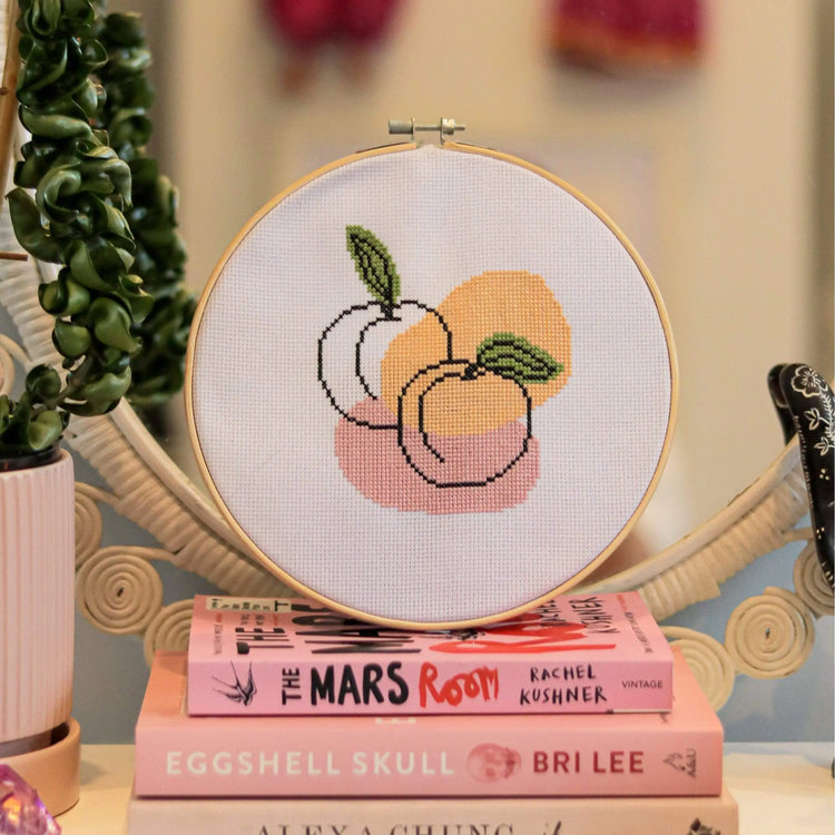 Craft Club Co PEACHY KEEN Cross Stitch Kit. The design is shown sitting on a stack of pink books.