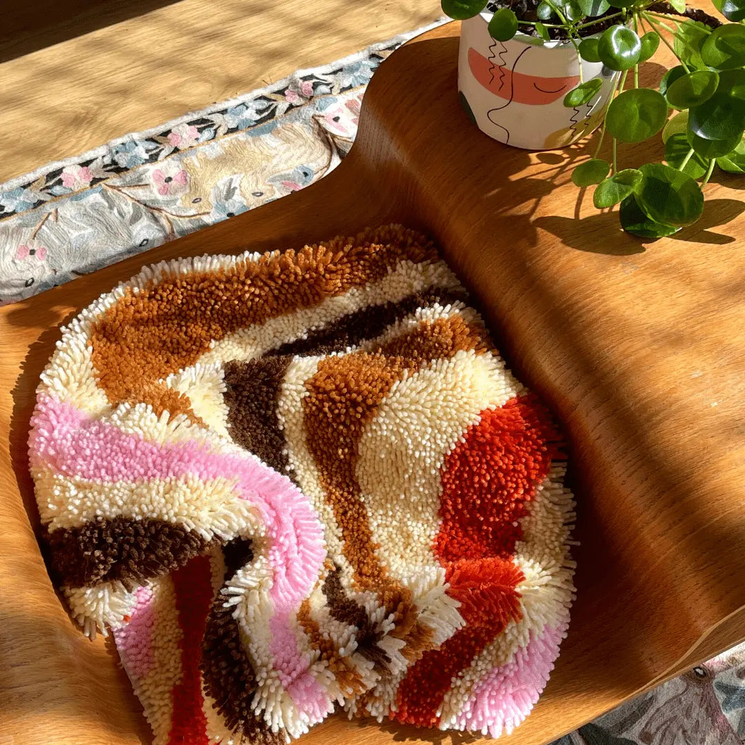 Craft Club Co CARAMEL SWIRL Rug Making Kit. The rug sits on a coffee table in the afternoon sun. The rug is scrunched up showing the individual pieces of yarn it is made from.