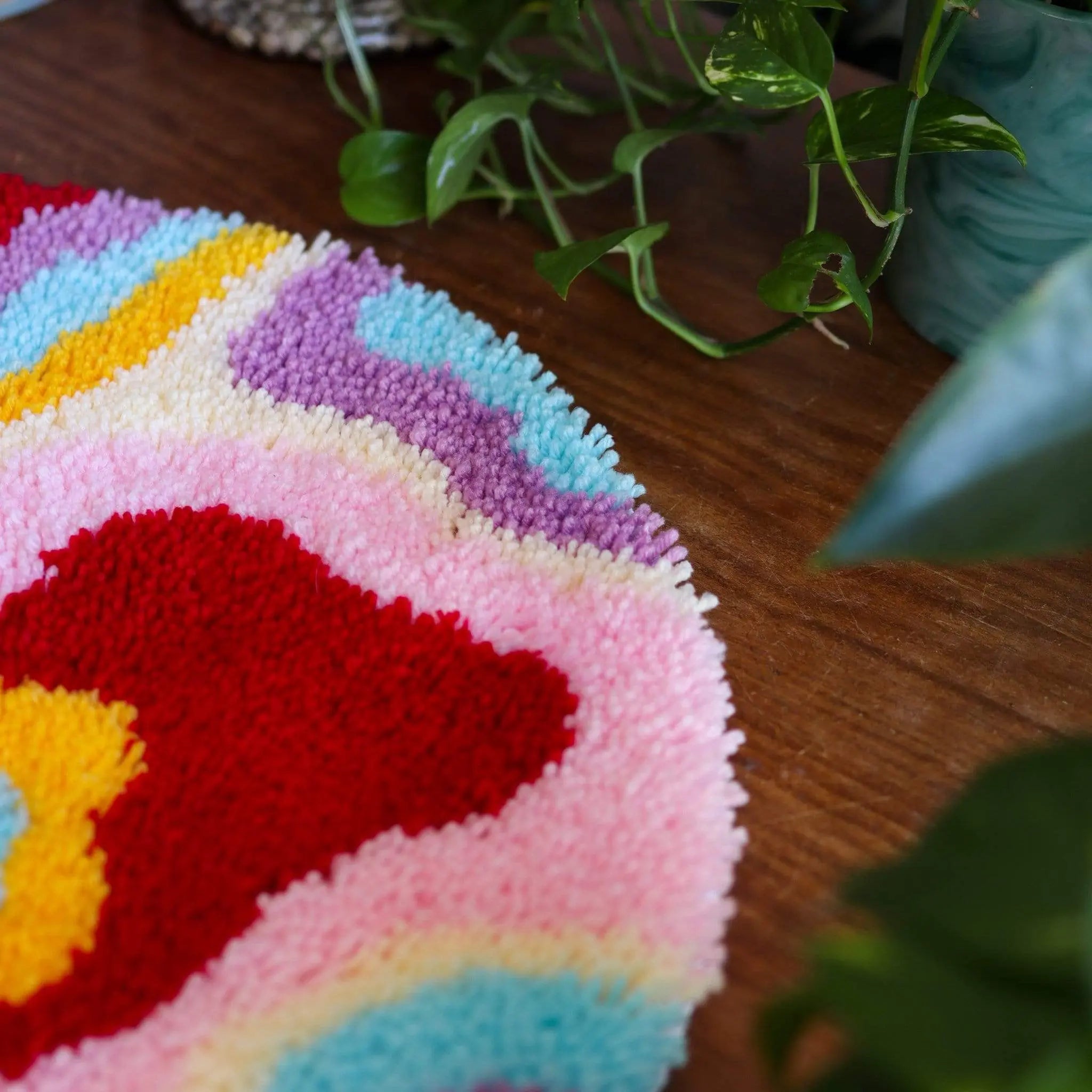 Craft Club Co PSYCHEDELIA Rug Making Kit. A close up of the upper left side of the rug, showing pink, red, purple and blue yarn.