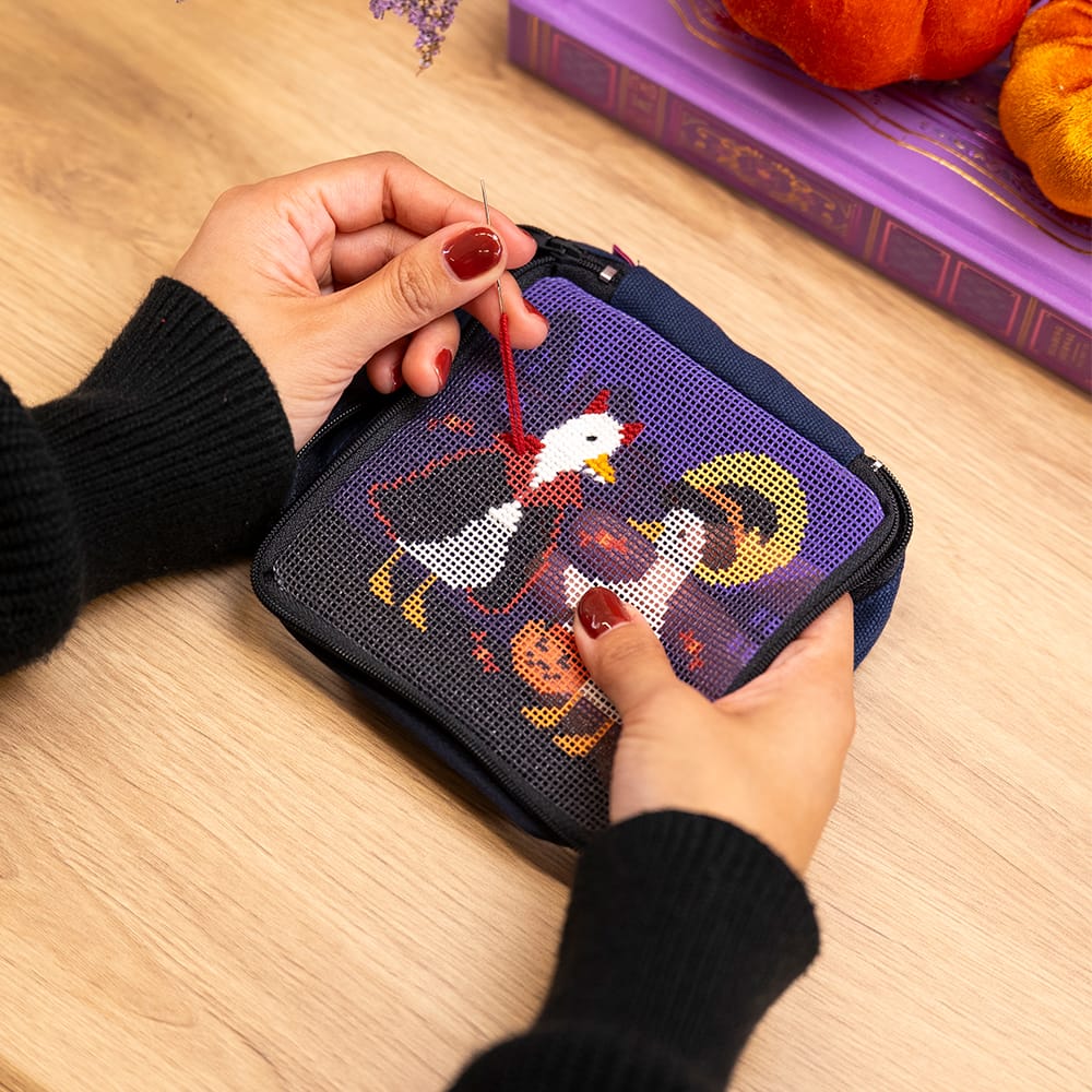 Hands stitching the TOIL AND TROUBLE pouch canvas with red thread