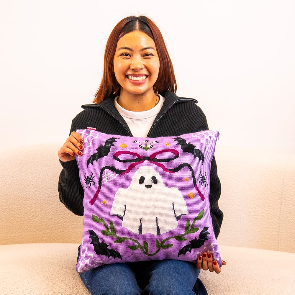 A maker holding the finished BOO-TIFUL ghost needlepoint cushion
