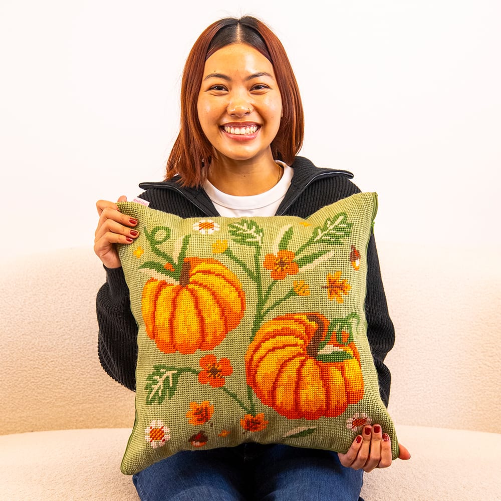 A maker holding the finished COTTAGE PUMPKINS needlepoint cushion