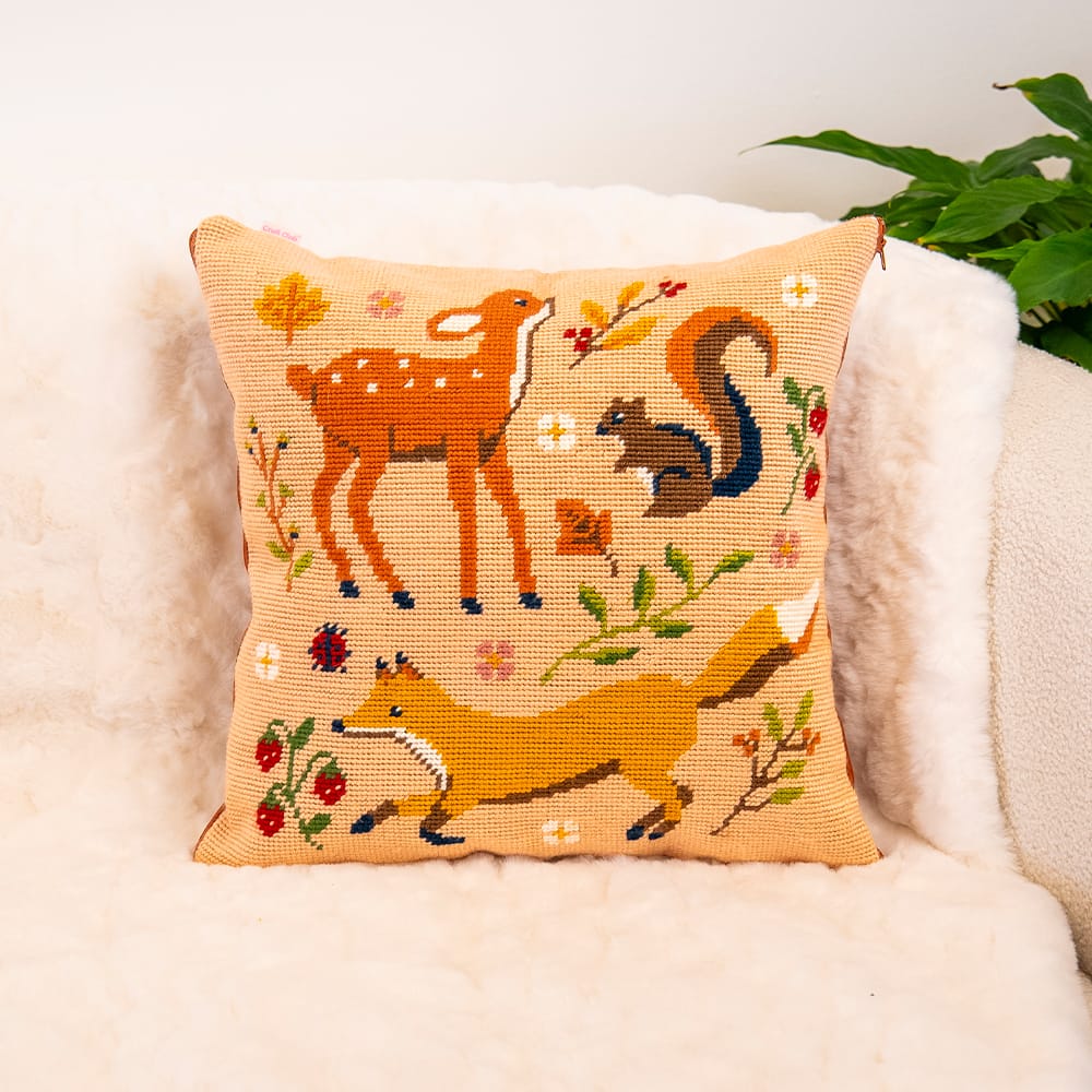 FALL FRIENDS woodland needlepoint cushion finished and styled on a cream sheepskin armchair