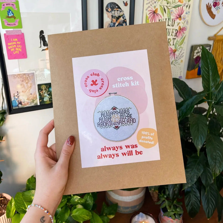 Craft Club Co ALWAYS WAS, ALWAYS WILL BE Cross Stitch Kit. A hand holds the kit in its packaging. The kit is packaged in an A4 craft envelope with a blush pink label. The label is a modern style with organic shapes.