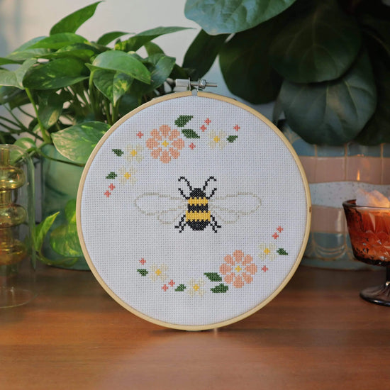 Craft Club Co BEE & BLOSSOM Cross Stitch Kit. The design shows a bee in the centre, made with black and yellow thread. The bee has metallic wings and is surrounded by blush, cream and pink flowers with green leaves.