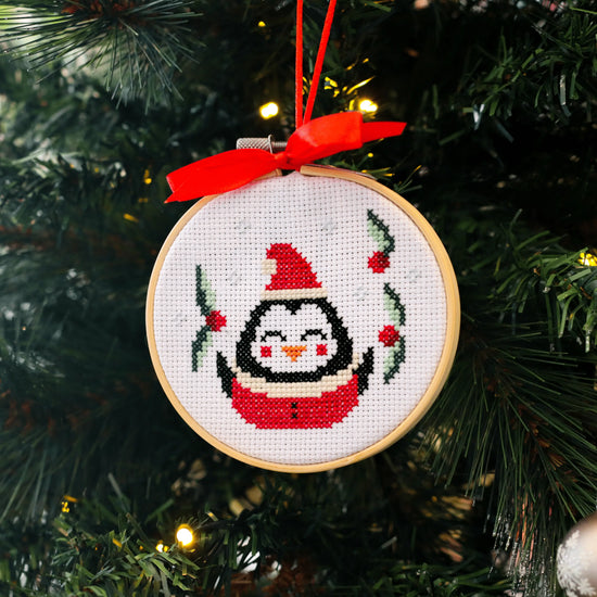 Craft Club Co CHRISTMAS MINI ORNAMENTS Cross Stitch Kit. Close up of the penguin kit, showing the stitching on the penguin and the holly around it.