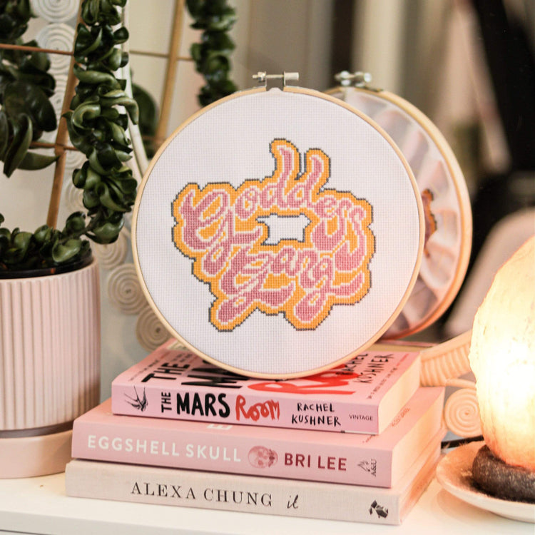 Craft Club Co GODDESS GANG Cross Stitch Kit. The design is shown on a pink stack of books with a salt lamp next to it.