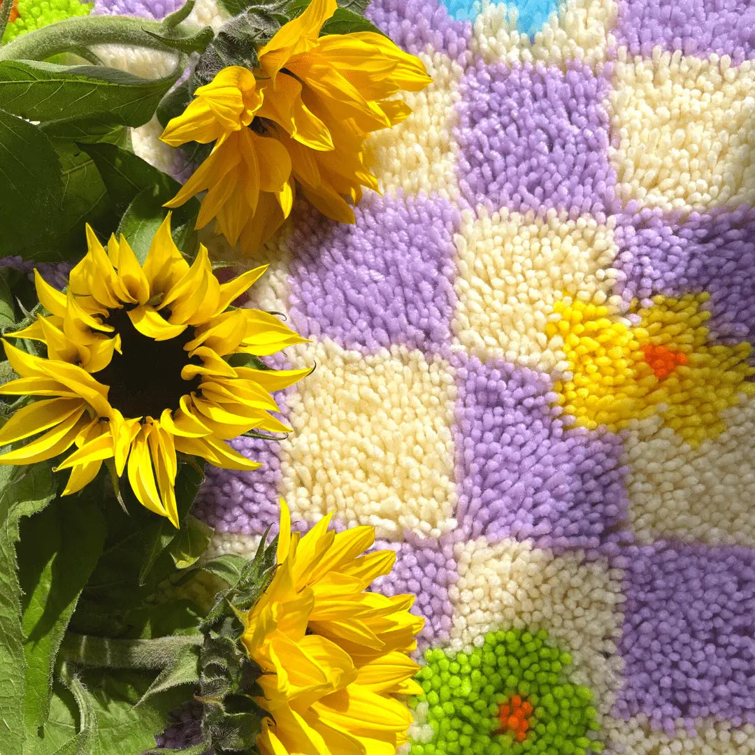 Craft Club Co CHECK ME OUT Rug Making Kit. An extreme close up of the rug showing the individual pieces of yarn. There are three sunflowers sitting on the rug in the sunlight.