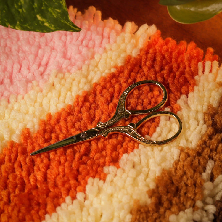 Craft Club Co Scissors. The scissors are shown sitting on the Caramel Swirl rug making kit. They nestle into the pieces of yarn.